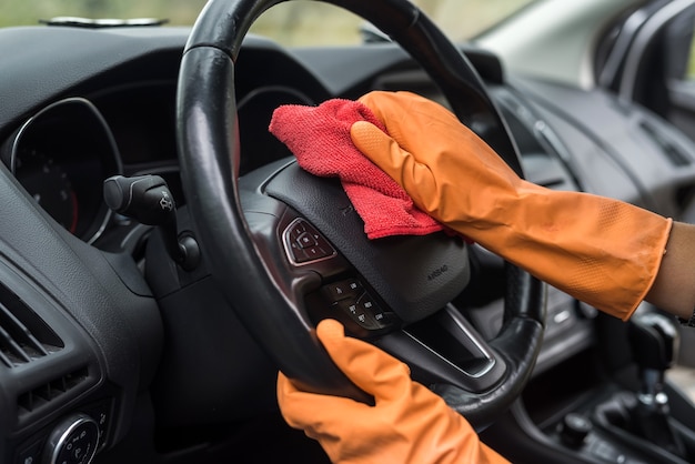 Vrouwelijke hand die haar auto-interieur schoonmaakt van coronavirus en pandemie met desinfecterende vloeistof. waswagen