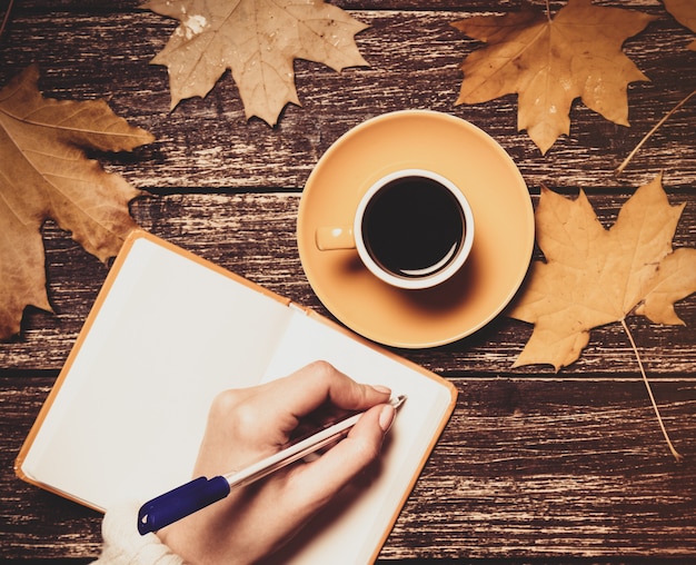 Vrouwelijke hand die iets schrijft in notitieboekje dichtbij kop van koffie.