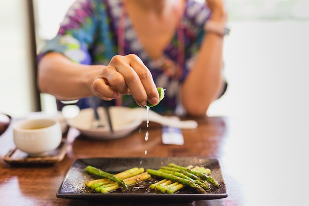 Vrouwelijke hand die limoen op gekookte asperges knijpt