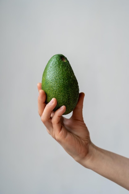 Vrouwelijke hand die rijpe organische avocado houdt tegen grijze muur