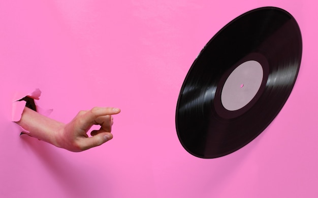 Foto vrouwelijke hand draait vinyl record door achtergrond van gescheurd roze papier. minimalistisch retro concept