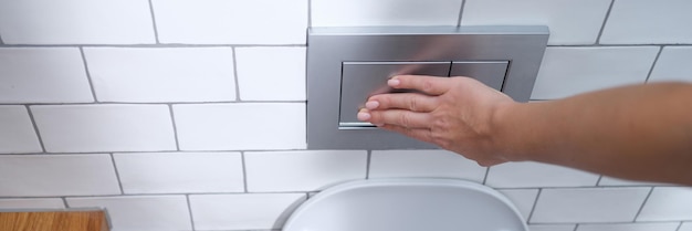 Vrouwelijke hand drukt op spoelknop in toiletclose-up