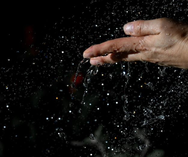 Vrouwelijke hand en vliegende druppels water op een zwarte achtergrond