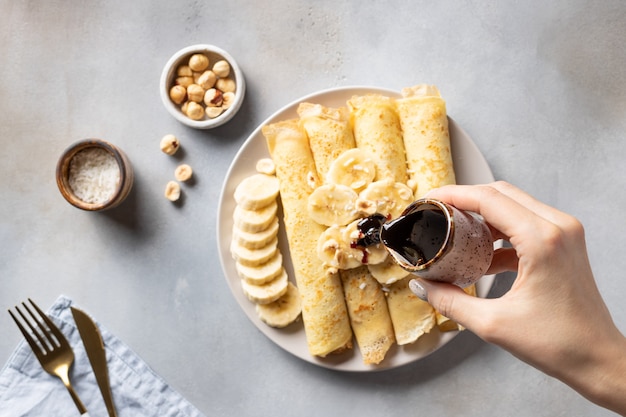 Vrouwelijke hand giet dadelsiroop over gerolde bananenpannekoeken