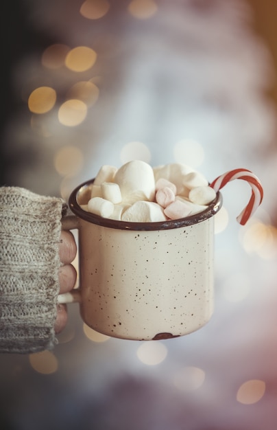 Vrouwelijke hand houden mok koffie met riet van het suikergoed en marshmallows