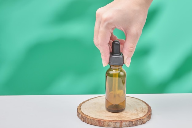 Foto vrouwelijke hand houdt cosmetisch product in buis glazen fles lotion anti-aging vochtinbrengende crème gezichtsolie of serum op groene achtergrond met lichte schaduw natuur schoonheid cosmetische huidverzorging concept