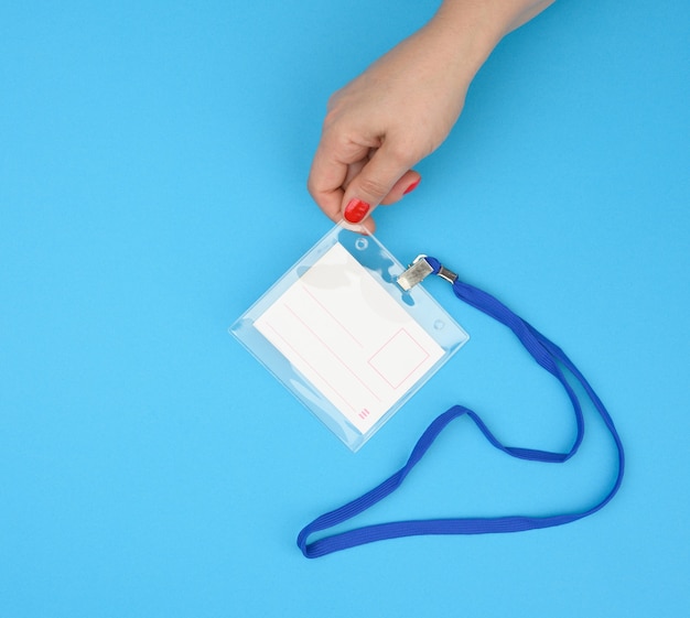 Vrouwelijke hand houdt doorzichtige plastic badge op een blauwe lanyard op een blauwe achtergrond, close-up