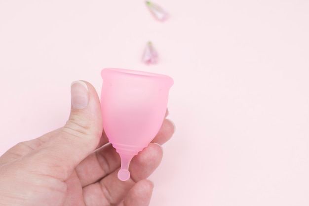 Vrouwelijke hand houdt een menstruatie cup op roze achtergrond. gezondheid van vrouwen, alternatief voor plastic afval, geen afval.