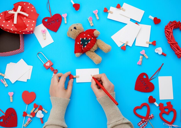 Foto vrouwelijke hand houdt een rood houten potlood en schrijft op een wit papier visitekaartje, naast kartonnen dozen