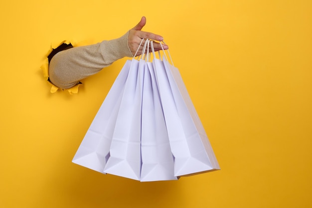 Vrouwelijke hand houdt een wegwerpzak van wit papier vast met handvatten voor boodschappen en kleding. Recyclebare verpakking. Zero waste. Uitverkoop