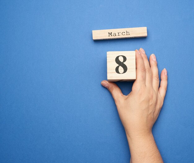 Vrouwelijke hand houdt houten kalender met datum van acht maart