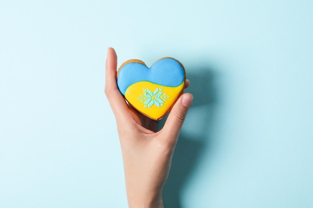 Vrouwelijke hand houdt koekje met Oekraïne vlag kleuren op blauwe achtergrond