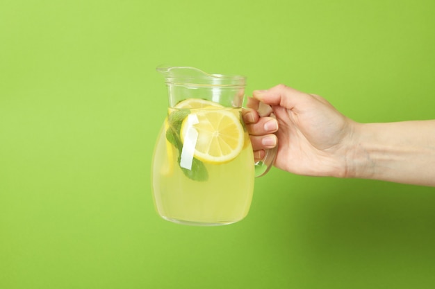 Vrouwelijke hand houdt kruik met limonade op groene achtergrond