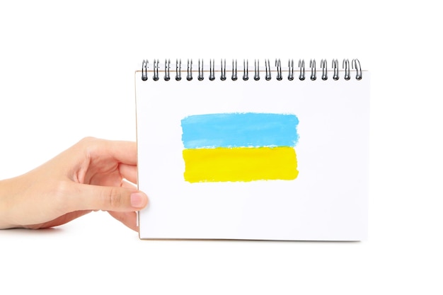 Vrouwelijke hand houdt notitieboekje met getekende Oekraïense vlag geïsoleerd op een witte achtergrond