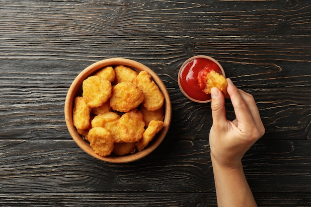 Vrouwelijke hand houdt nugget over de houten achtergrond met kom met nuggets