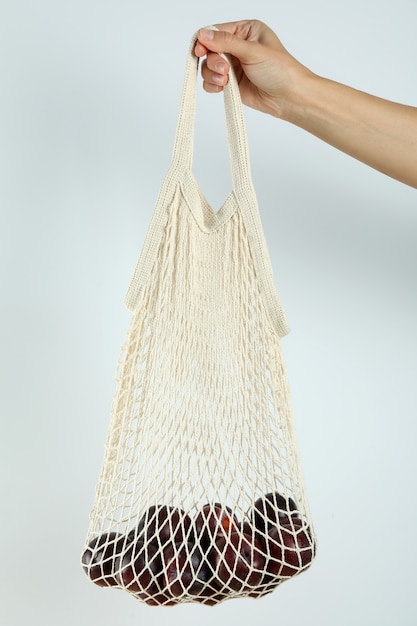 Vrouwelijke hand houdt string tas met pruimen op witte achtergrond.