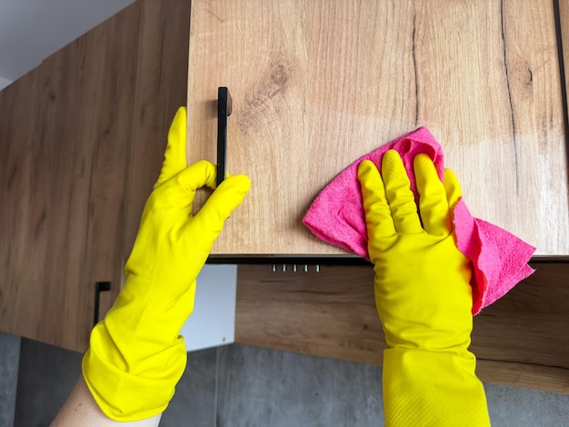 vrouwelijke hand in gele rubberen handschoenen met behulp van een doek schoonmaken van de houten top keuken