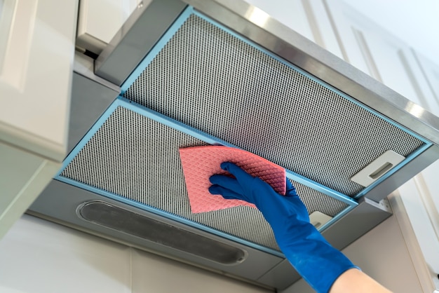 Vrouwelijke hand in rubberen beschermende Ã'Â scheve afzuigkap met doek in de keuken.
