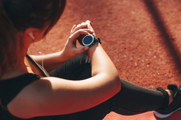 Vrouwelijke hand kijkt naar haar sporthorloge na het doen van cardio omdat ze 's ochtends buiten in een sportpark het dragen verliest terwijl ze op de grond rust.