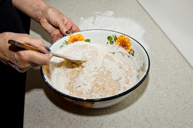 Foto vrouwelijke hand knetelt deeg uit melk van boter en meel in een metalen kom met een houten klop in de keuken