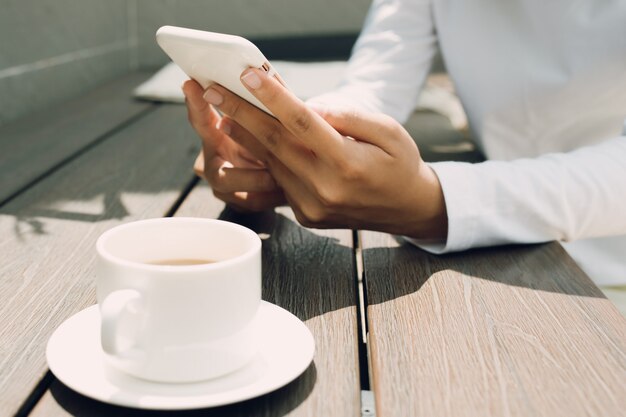 Vrouwelijke hand met behulp van mobiele telefoon over houten tafel bij coffeeshop