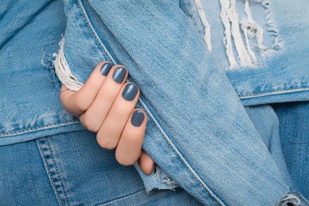 Vrouwelijke hand met blauw spijkerontwerp op het blauwe haveloze oppervlak van de denimstof.