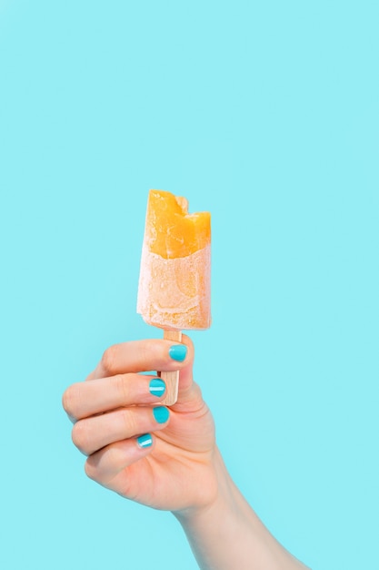 Vrouwelijke hand met blauwe nagellak met oranje ijs op blauwe achtergrond