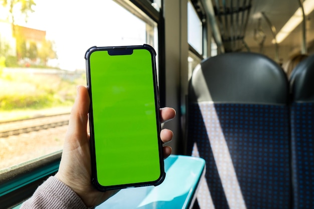 Vrouwelijke hand met chroma key-schermtelefoon in de trein Sociaal netwerk Werk- en reistelefoon met leeg kopieerruimtescherm voor uw sms Nieuwe apps Smartphone met groen scherm Mock Up Display