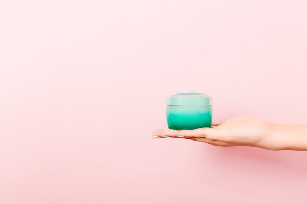 Vrouwelijke hand met crème fles lotion geïsoleerd. Meisje geeft pot cosmetische producten op roze achtergrond.