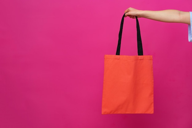 Vrouwelijke hand met eco of herbruikbare boodschappentas tegen roze achtergrond