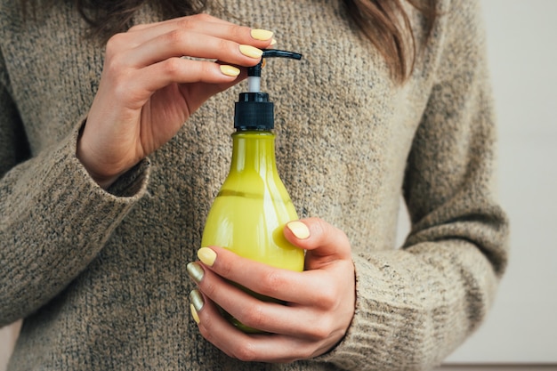 Vrouwelijke hand met een gele manicure die groene fles met kosmetische room houdt