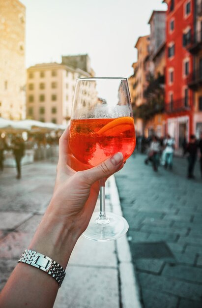 Vrouwelijke hand met een glas oranje cocktail spritz bij oude gebouwen Zonnige dag in Verona Italië