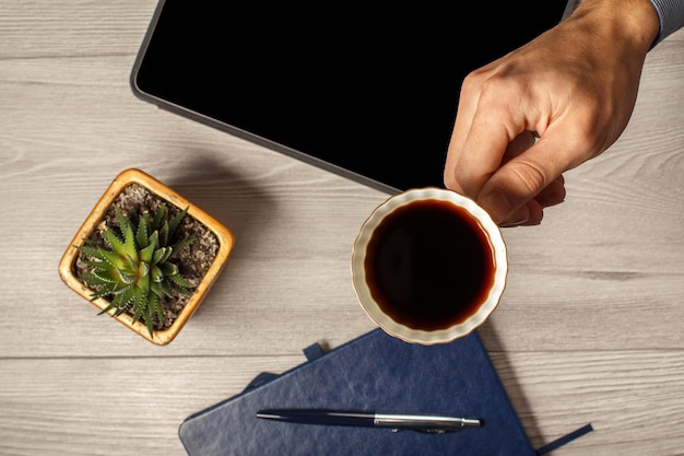 Vrouwelijke hand met een kopje koffie met notitieboekje op de achtergrond