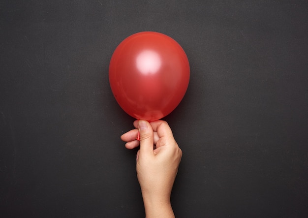 Vrouwelijke hand met een opgeblazen rode luchtballon op zwart