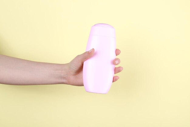 Vrouwelijke hand met fles cosmetisch product voor douche op gekleurde achtergrond