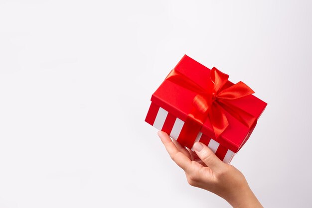 Vrouwelijke hand met gestreepte geschenkkist met rood lint op witte achtergrond Kerstmis Nieuwjaar Valentijnsdag en verjaardag concept kopieerruimte