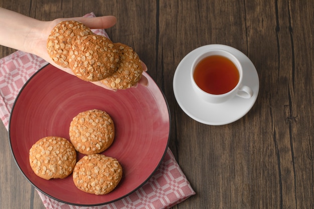 Vrouwelijke hand met havermoutkoekjes met zaden en granen die op rode plaat worden geplaatst