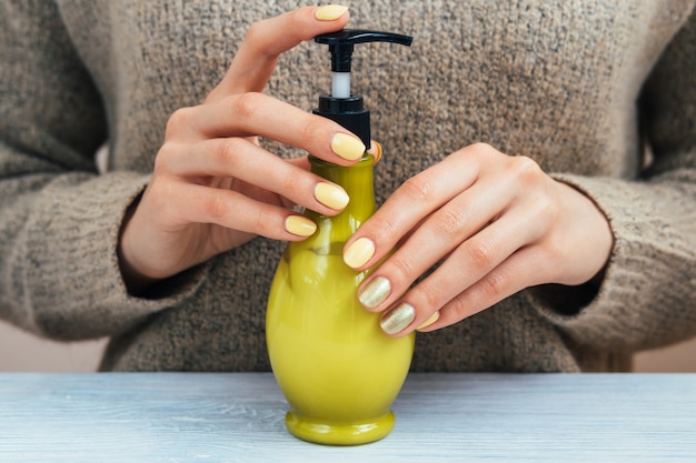 Vrouwelijke hand met heldere manicure die groene fles met kosmetische room houdt