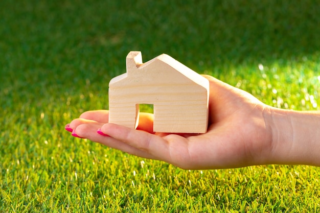 Vrouwelijke hand met houten huis model boven het gras close-up