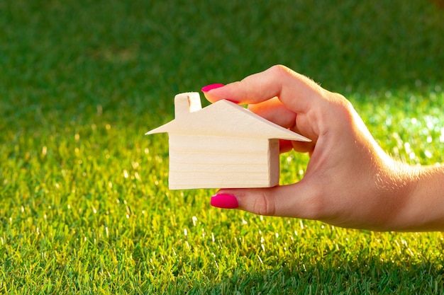 Vrouwelijke hand met houten huis model boven het gras