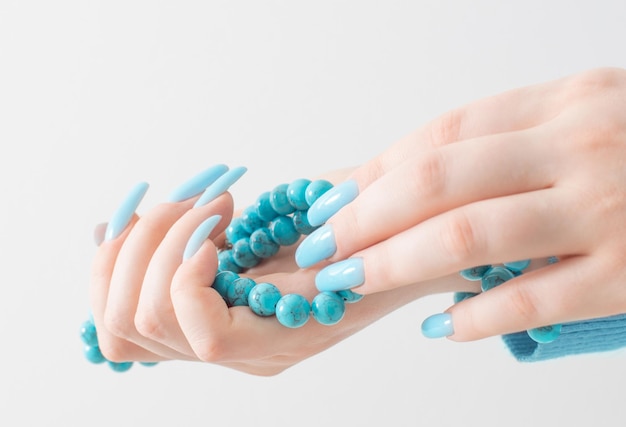 Vrouwelijke hand met manicure en turquoise kralen op witte achtergrond