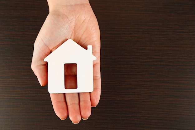 Vrouwelijke hand met model van huis op houten tafel achtergrond