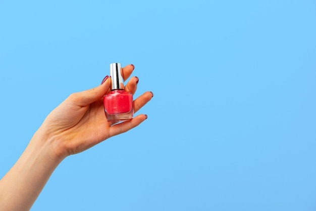 Vrouwelijke hand met nagellak tegen blauwe achtergrond close-up