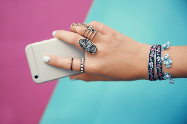 Foto vrouwelijke hand met sieraden en mobiele telefoon op kleur achtergrond