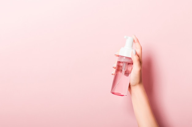 Vrouwelijke hand met spray crème fles lotion geïsoleerd. Het meisje geeft cosmetische producten op roze