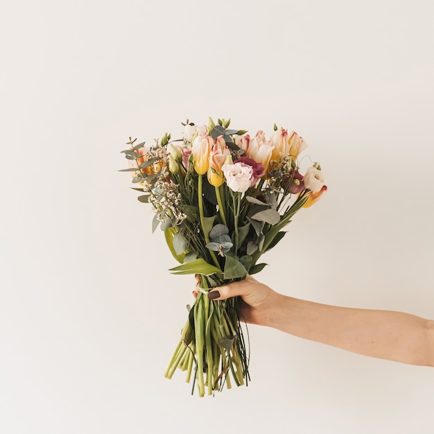 Vrouwelijke hand met tulp bloemen boeket tegen witte muur