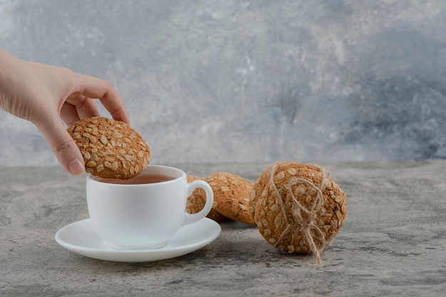 Vrouwelijke hand met vers koekje bovenop zwarte thee.