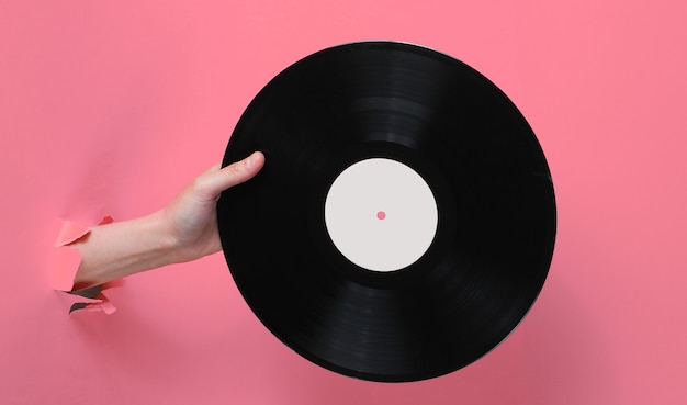 Vrouwelijke hand met vinyl record door de gescheurde roze papieren achtergrond. Minimalistisch retro concept