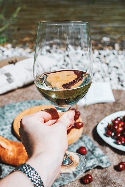 vrouwelijke hand met wit wijnglas aan de rivierkust en romantische picknickachtergrond