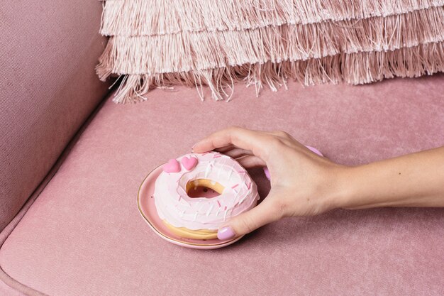 Vrouwelijke hand neemt een zoete roze donut op een roze oppervlak